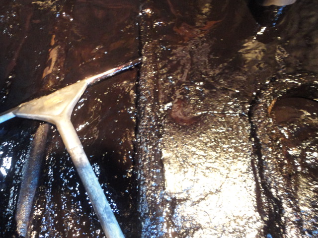 タンク内部にこびり付いたスラッジを器具を使いこそぎ落とす作業の写真